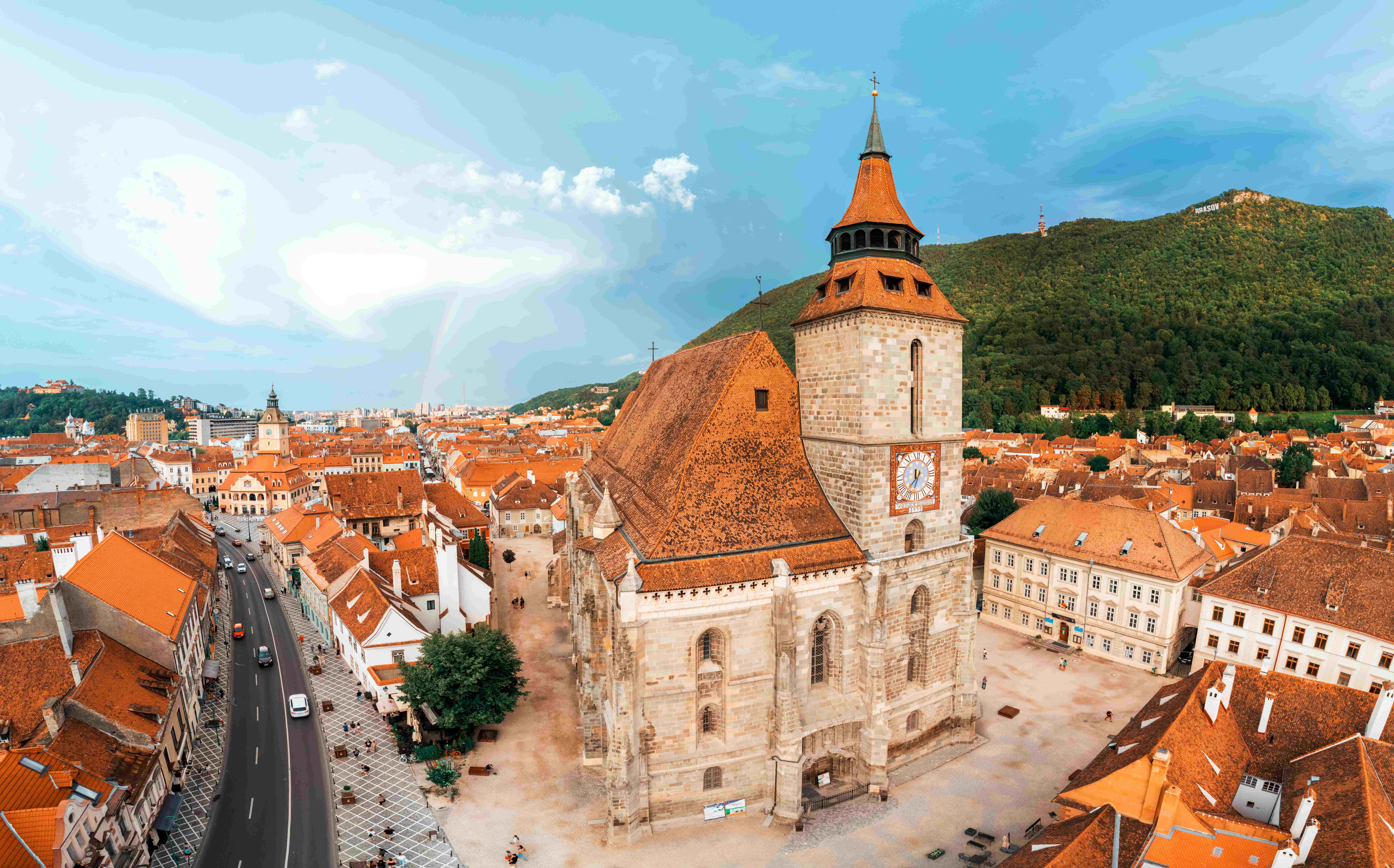 aerial drone panoramic view black church old brasov centre romania old residential buildings around it narrow streets with moving cars hills with greenery